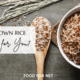 A bowl of brown rice on a cloth, next to a wooden spoon of the rice