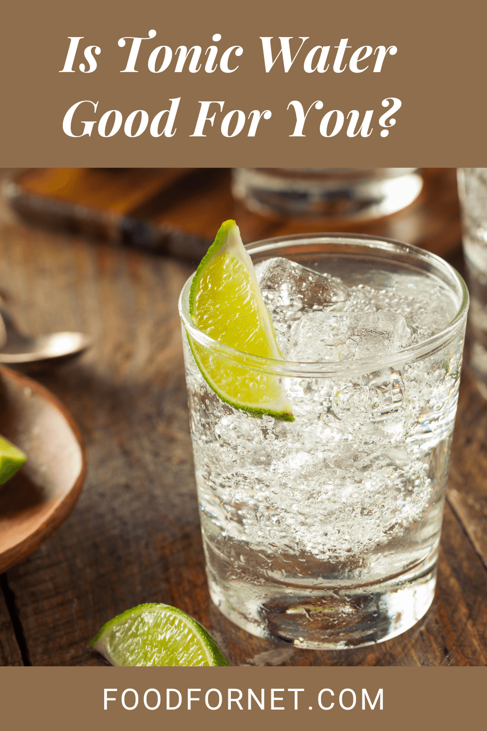 Two glasses of tonic water with ice and a lime, on a wooden table where there are some limes and a plate of cut up limes