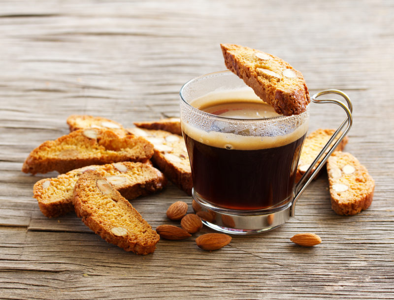 Various pieces of Italian biscotti next to a cup of espresso with one resting on top of the cup