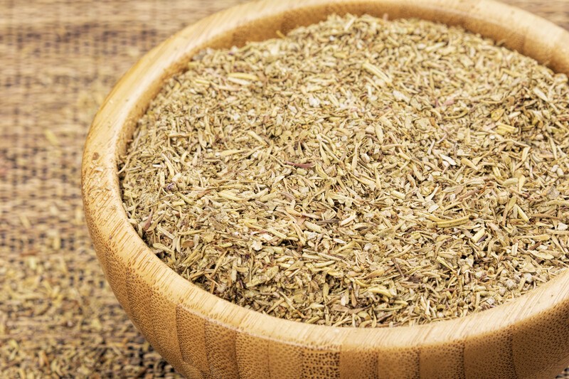 a closeup image of a wooden bowl full of Italian seasoning resting on a pile of Italian seasoning