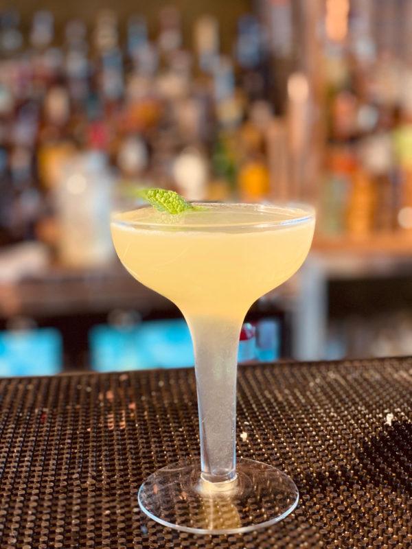 A yellow cocktail in a glass on a bar