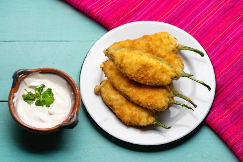 A small white plate that contains grilled jalapeno poppers next to a bowl of white dipping sauce