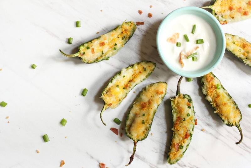 A white table seven jalapeno poppers next to a blue bowl of dip