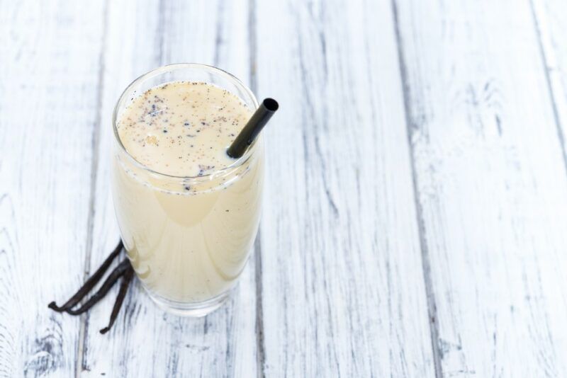 A white wooden table with a glass of Guinness milk punch and some vanilla beans