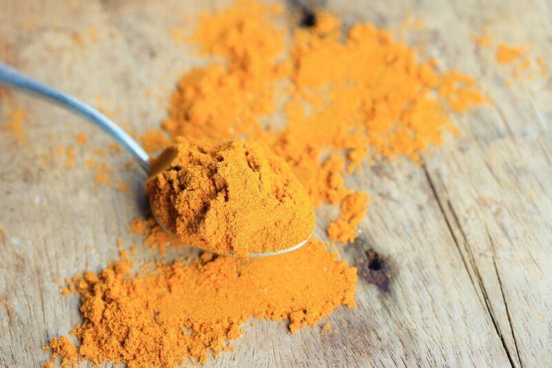 on a rustic looking wooden surface is a spoon full of Jamaican curry powder, with loose Jamaican curry powder around it