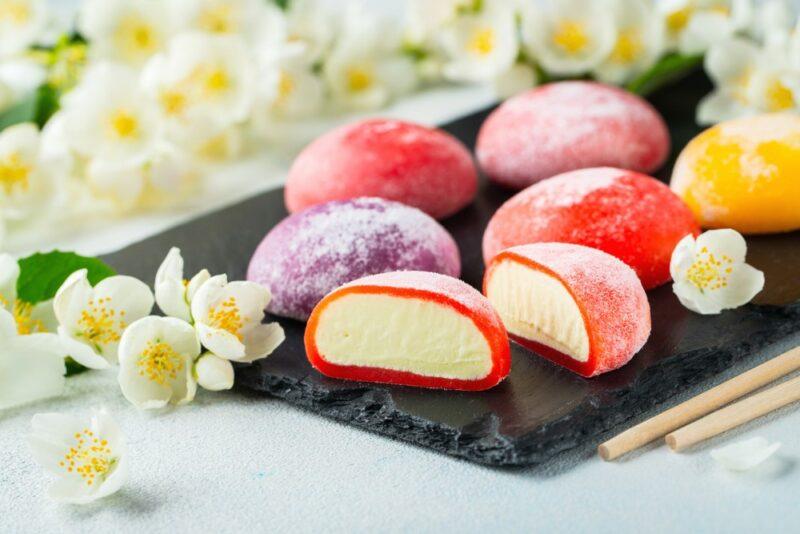 A small black tray containing various flavors of Japanese mochi ice cream, one that has been sliced open