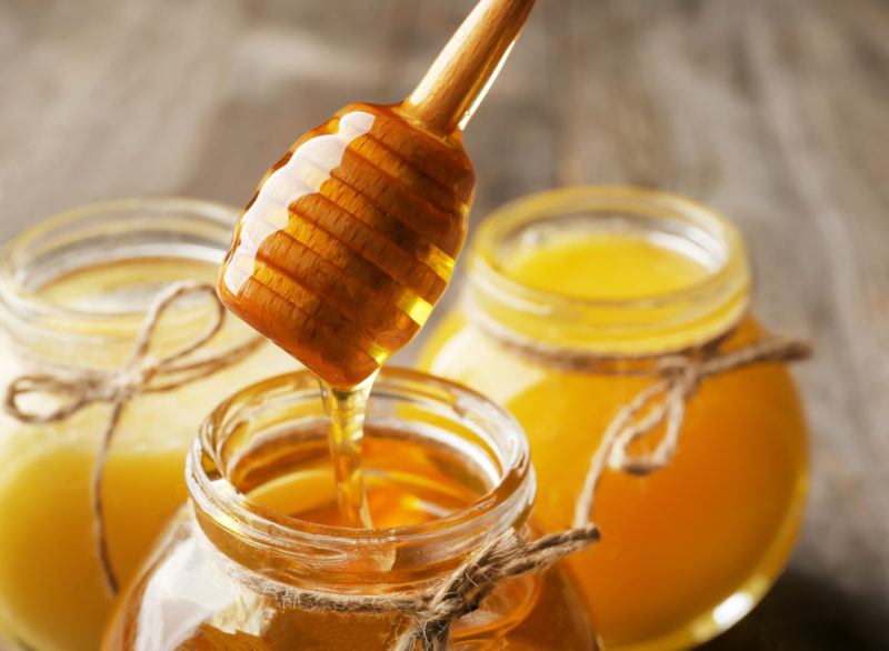 Three jars of honey with a stick