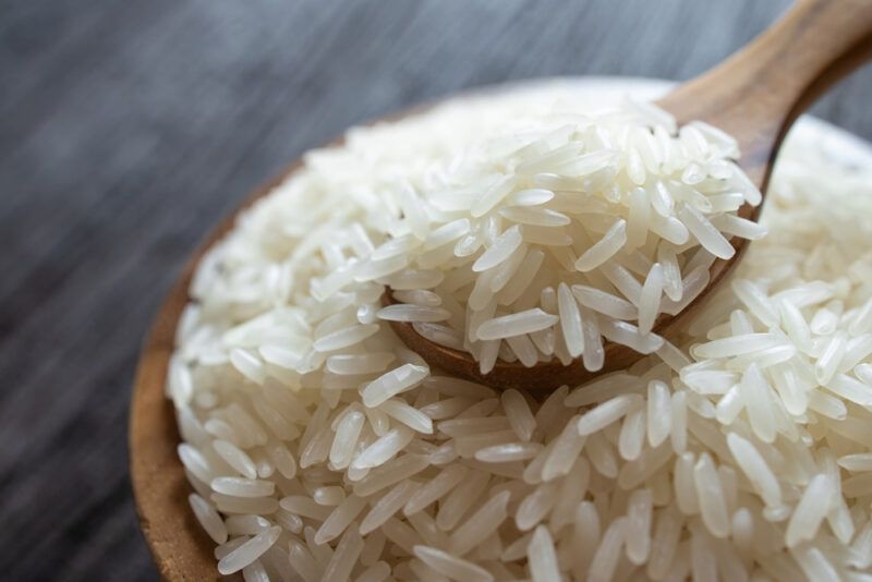 on a dark wooden surface is a wooden brown bowl full of Jasmine rice