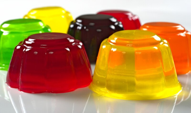 Nine molded gelatin deserts in red, yellow, orange, green, and purple rest on a white reflective surface.