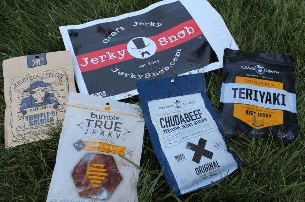 Four bags of jerky on the grass with a packet from the company