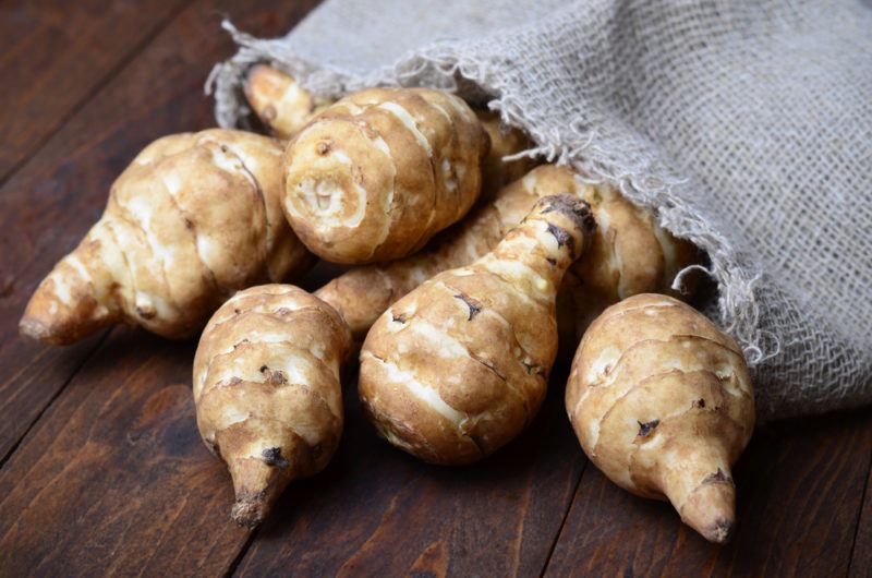 A selection of Jerusalem artichokes spilling out onto a wooden table