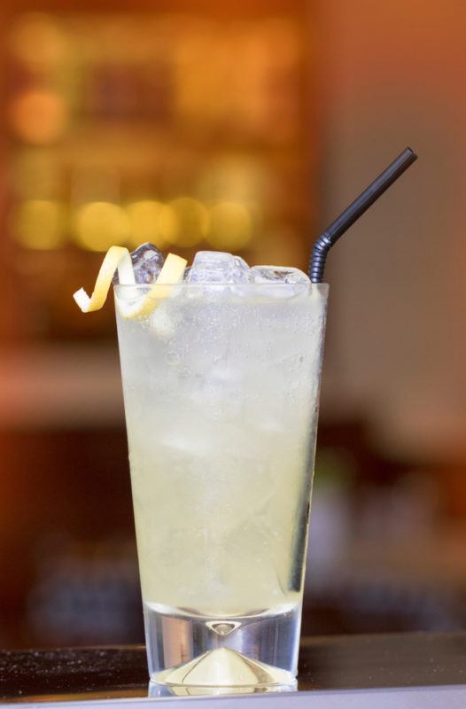 A tall John Collins cocktail with a blurred image of a bar in the background