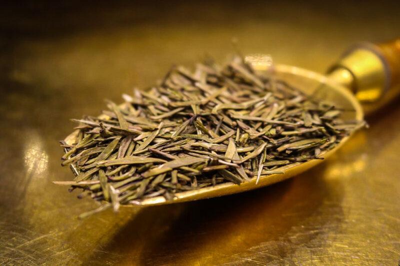 on a wooden surface is a gold metal scoop with loose Jun Shan Yinzhen tea