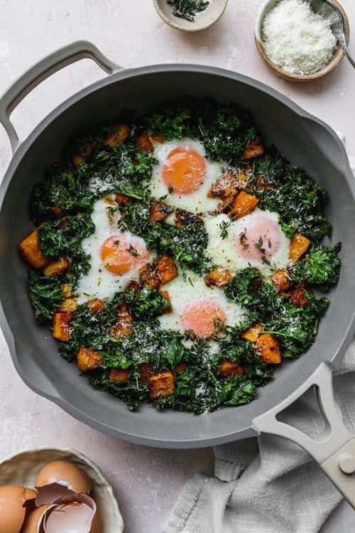 A frypan containing a kale butternut squash breakfast hash with eggs