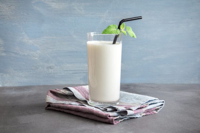 A glass of kefir on a table with a straw against a blue background