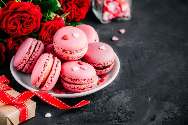 A dark table with ketchup macrons, roses, and gifts