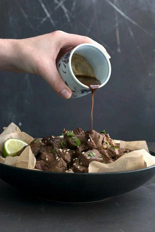 Someone pouring dressing over Asian steak bites