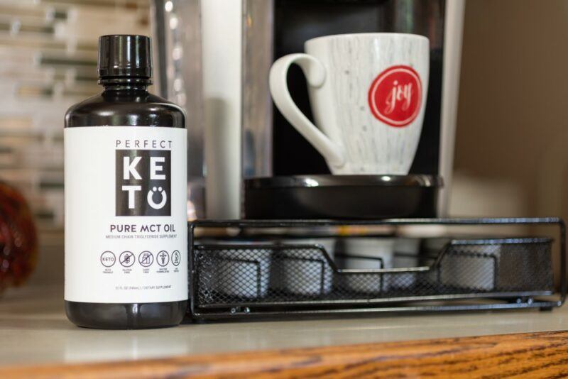 A bottle of KETO brand MCT oil next to a coffee cup and related products