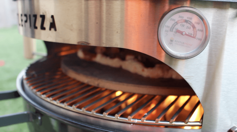 kettlepizza charcoal grill cooking pizza at over 700 degrees fahrenheit shown on temperature gauge