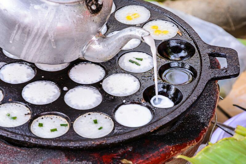 A black pan with half spheres, being used to make a khanom kroc dessert