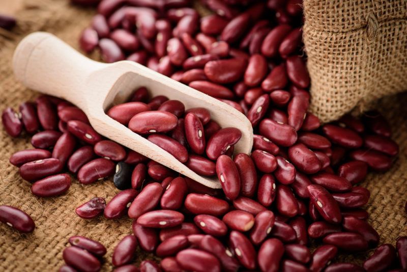 A bag of kidney beans spilling onto the table with a wooden spoon of beans