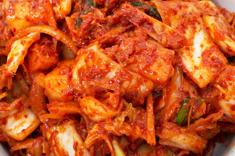 This photo shows a closeup of kimchi, including pieces of cabbage and the red pepper sauce.