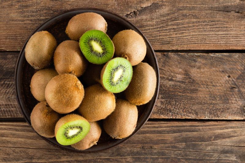 A black bown containing kiwis and a couple of sliced kiwis