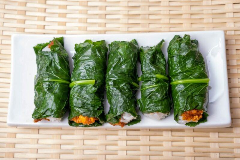 A woven cloth mat with a white plate that contains five Korean lettuce wraps that are known as ssambap