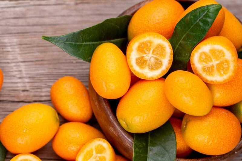 Orange kumquats and leaves on a wooden table. Most a whole but a few have been sliced in half