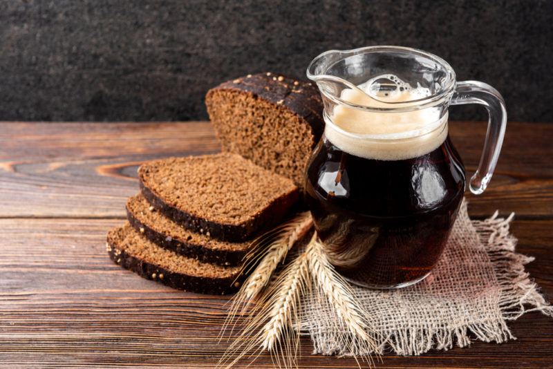 A jug of Kvass, some bread and some wheat on a wooden table