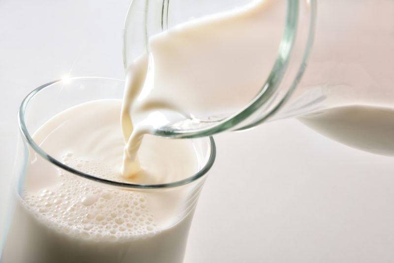 A glass of lactose free milk being poured from a jug