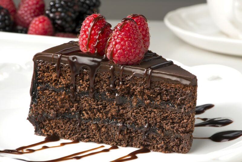 A layered chocolate cake with chocolate icing and a few raspberries on top