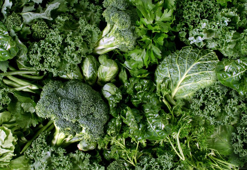 Several types of dark green leafy vegetables fill this photo, including broccoli, kale, and spinach.