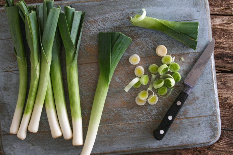 Four or five whole leeks and some sliced leeks on a cutting board