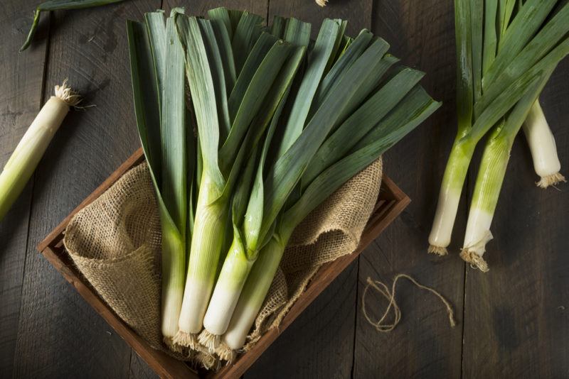 A wooden box with a cloth that contains fresh leeks and more leeks on a woodent table