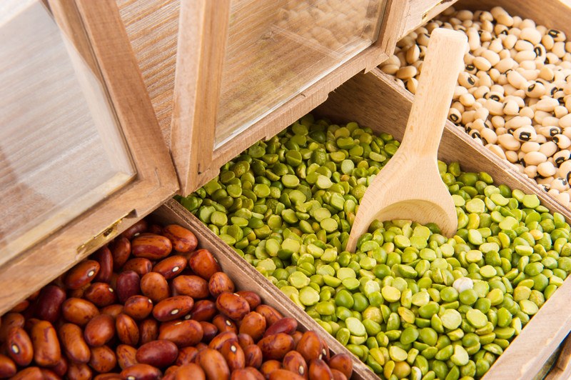 This photo shows three side by side bulk bins filled with pinto beans, split peas, and blackeye peas.