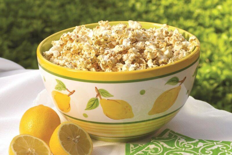 A yellow and white bowl with lemons, containing lemon poppy seed popcorn