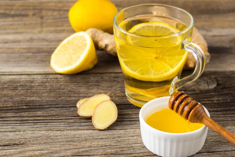 A glass mug of lemon, honey and giner tea with the ingredients seperately on a wooden table