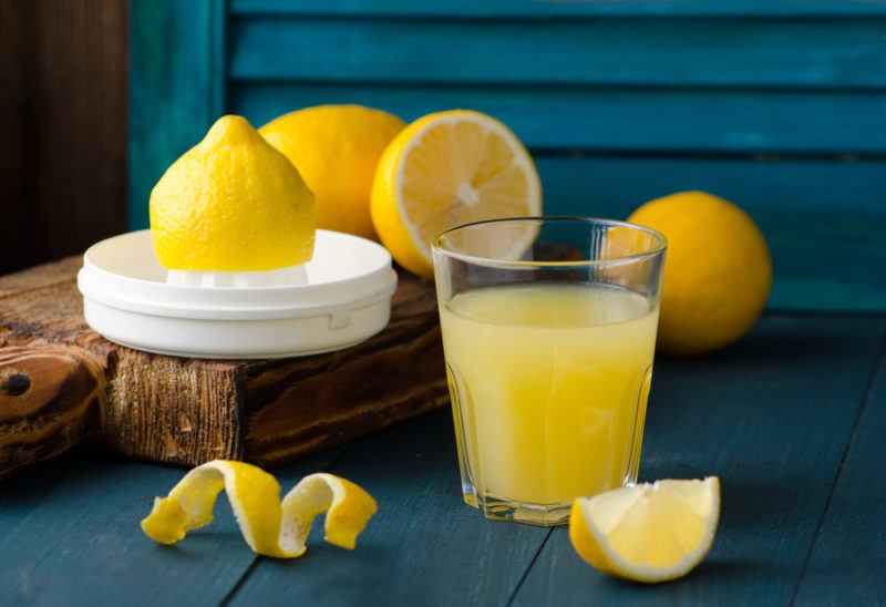 A glass of lemon juice, next to a squeezer and some cut lemons