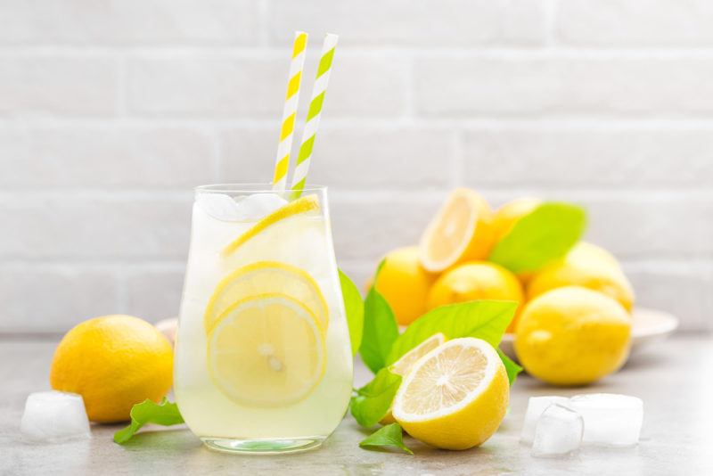 A glass of lemon water with straws on a table with many lemons