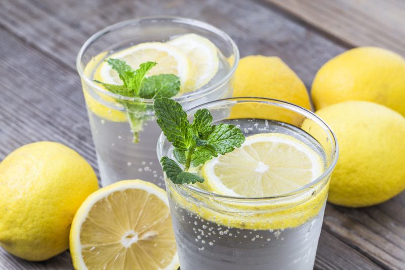 Two glasses of lemon water with mint, along with variou lemons