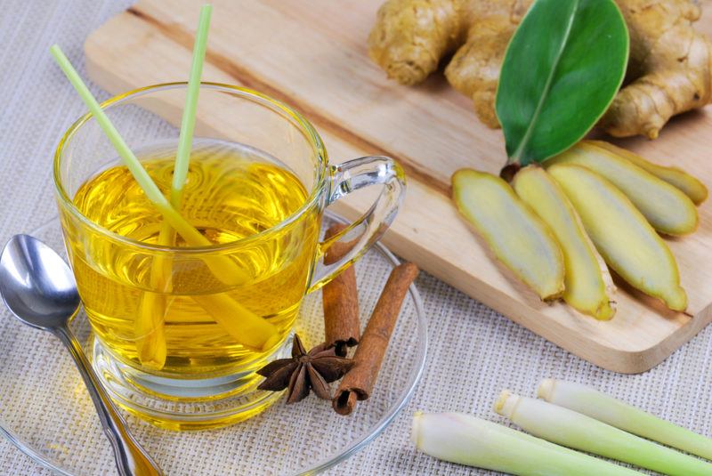 A glass mug of lemongrass tea next to lemongrass, some of which has been cut