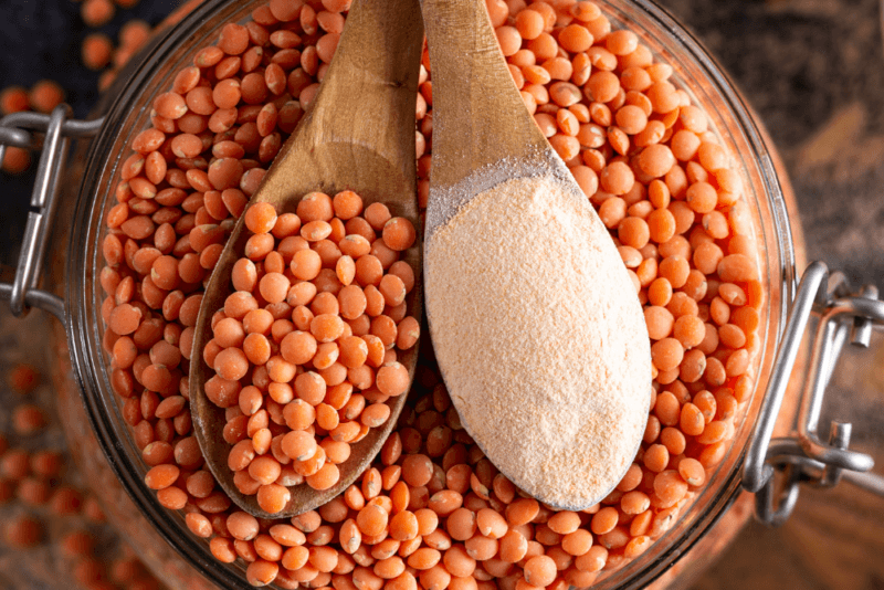 A large bowl of red lentils with a wooden spoon of red lentils and another of lentil flour