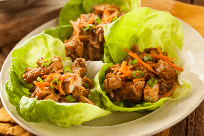 A white plate with a few lettuce wraps that include chicken and shredded carrot