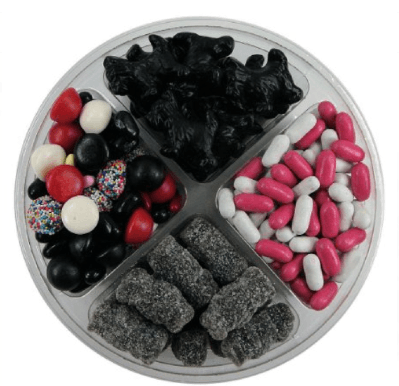 Round plastic container divided into four sections each with a different variety of licorice.   From left to right assorted, black Scotties, candy coated, and sugar coated black licorice bears