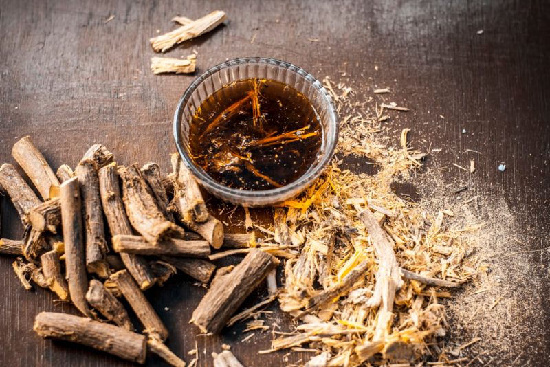 A mug of licorice root tea with dried licorice roots on the table.