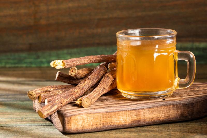 A mug of licorice tea with licorice roots on a wooden board