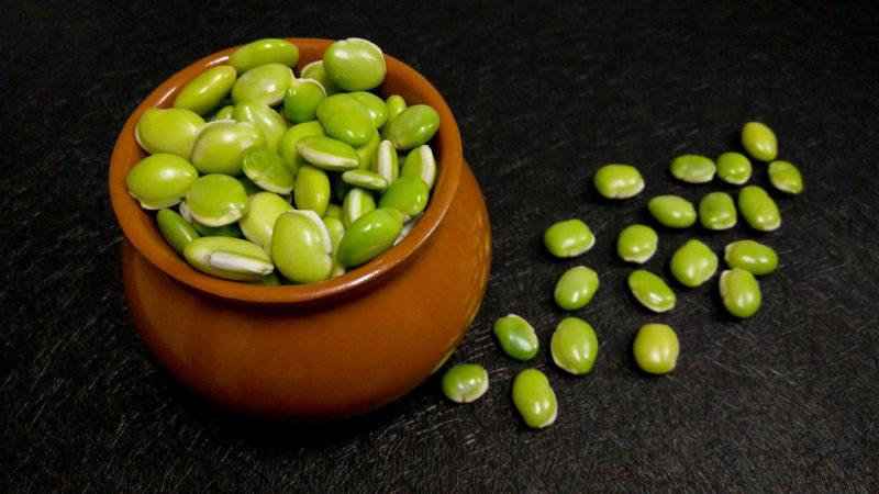 A brown bowl of lima beans and more lima beans on a table