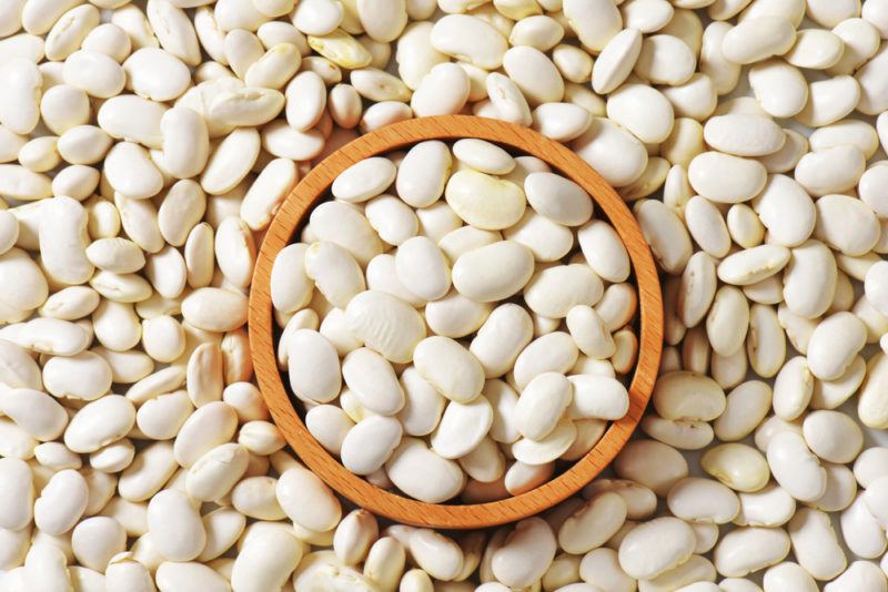 Lima beans on a table with a wooden bowl of lima beans on top