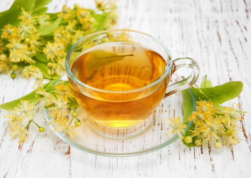 A glass of brown linden tea, surrounded by fresh linden flowers